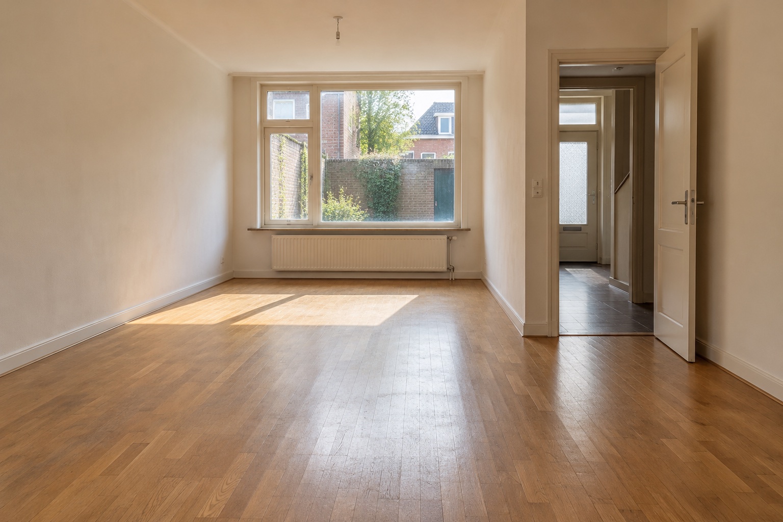 Sfeerbeeld van een lege, geveegde woonkamer met houten vloer en natuurlijk daglicht